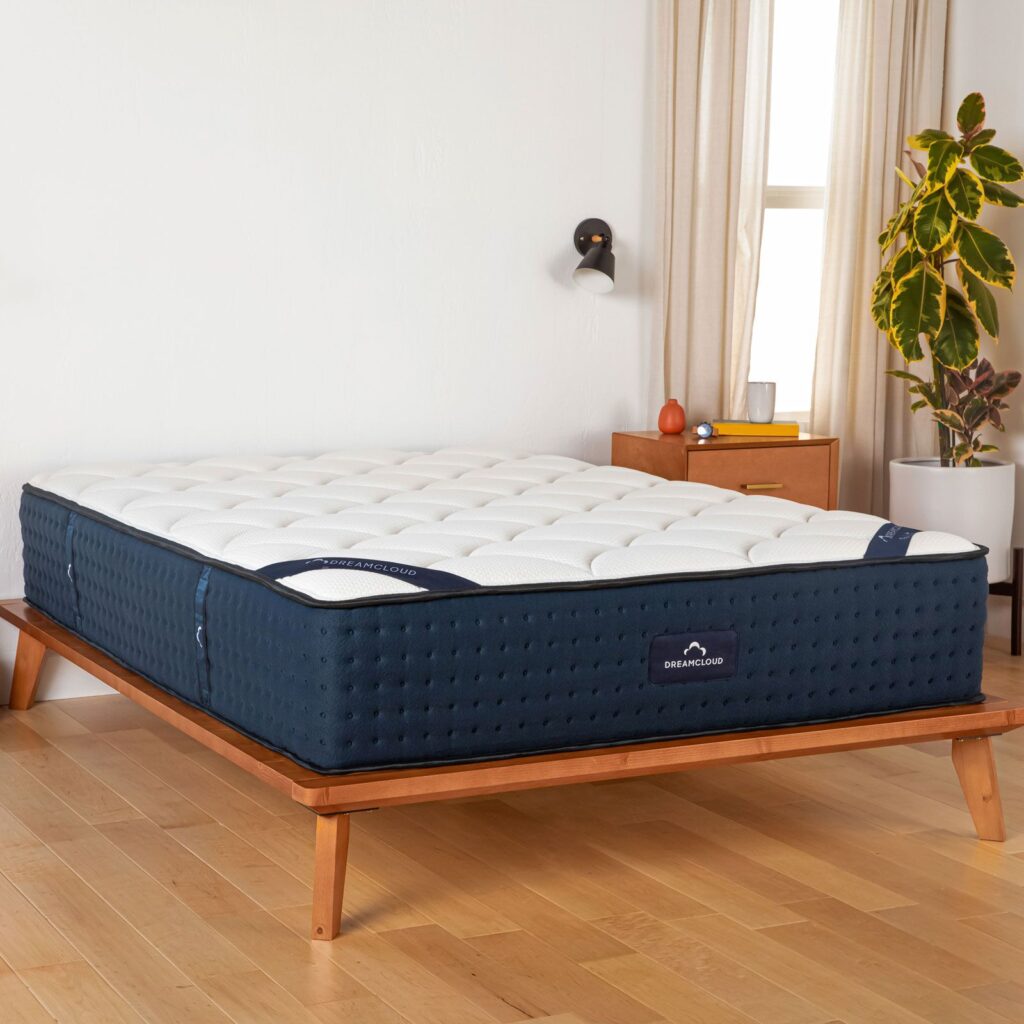 DreamCloud mattress on a wooden platform bed in a bright room with natural light, featuring a plush white top and dark blue sides, emphasizing luxury and comfort.