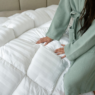 Woman in a green robe touching a plush, high-loft bamboo duvet comforter on a bed, emphasizing comfort and luxury associated with DreamCloud bedding products.