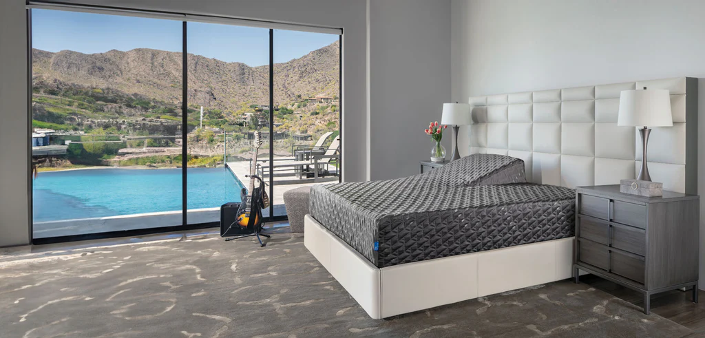 Strada Hybrid Medium mattress on a modern bed frame in a spacious bedroom with large windows showcasing a scenic outdoor view of mountains and a swimming pool, emphasizing comfort and relaxation.