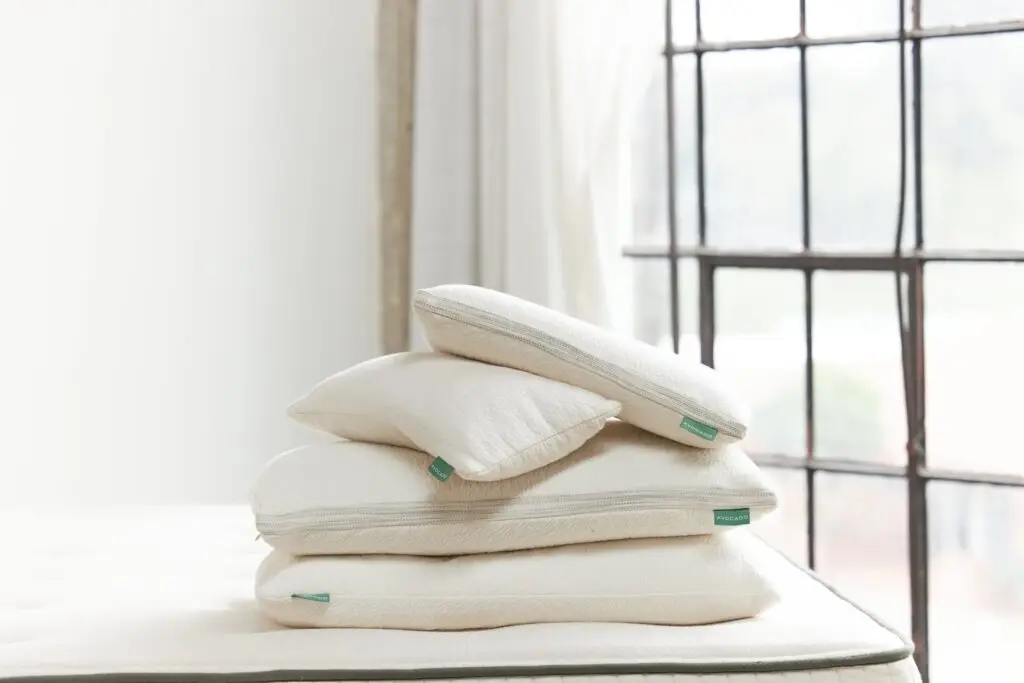 Stack of various pillows on a mattress, emphasizing different pillow types for optimal sleep support, with natural light from a window in the background.