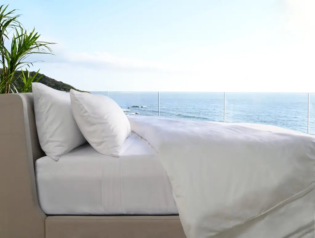 Bed with white sheets and pillows, overlooking a serene ocean view, highlighting comfort and style for bedroom aesthetics.