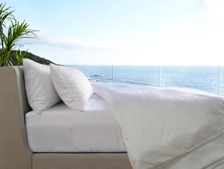 Bed with white sheets and pillows overlooking a serene ocean view, highlighting comfort and tranquility for sleep.
